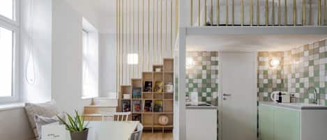 A compact hotel room with a dining area, kitchenette, and a bookshelf.