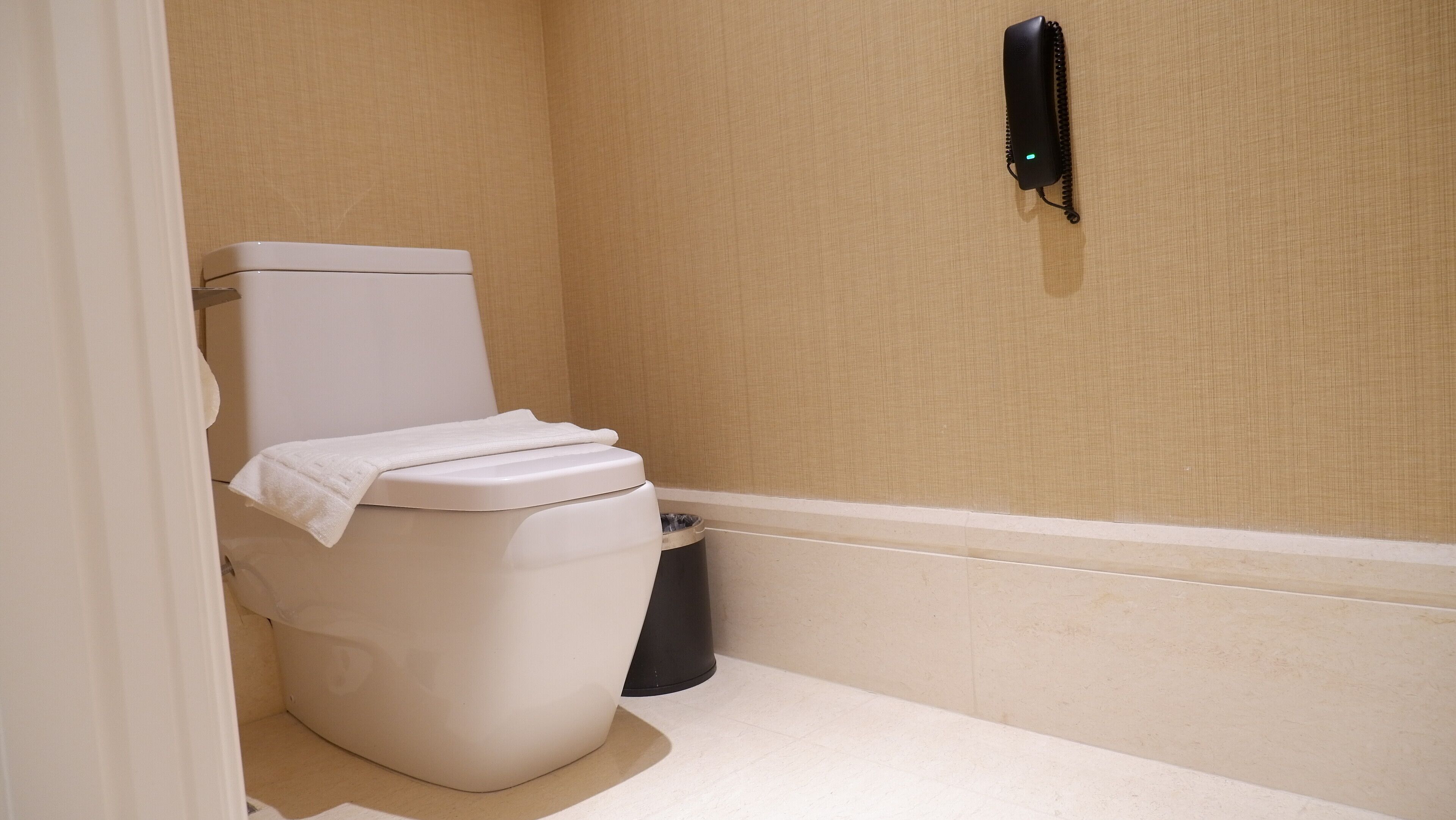 A small, clean bathroom with a toilet, a trash bin, and a wall-mounted telephone.