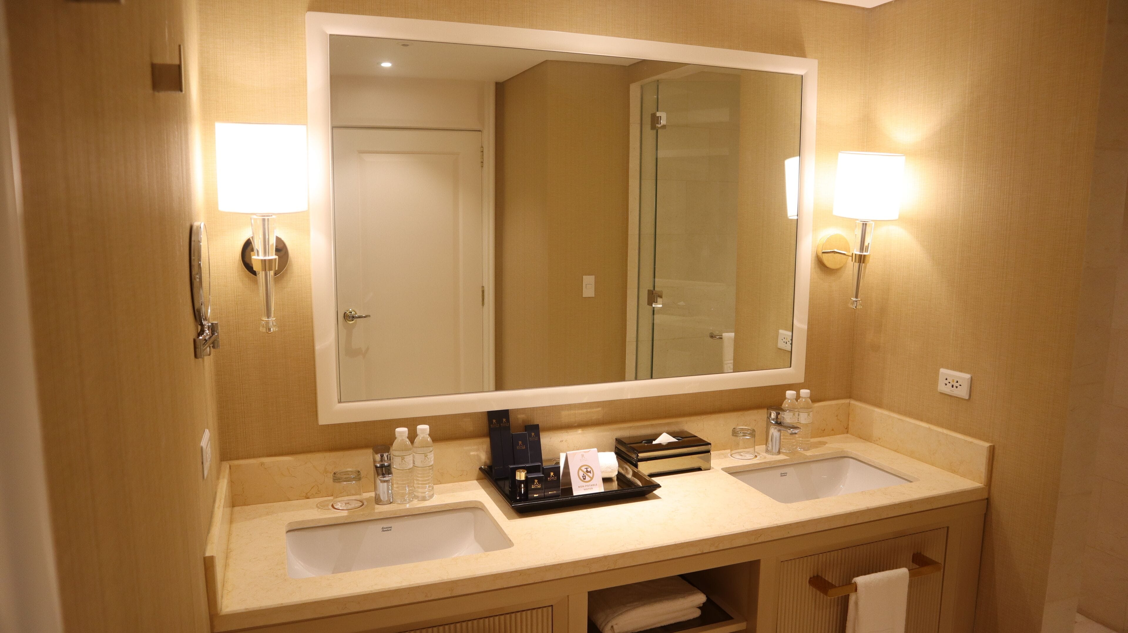A hotel bathroom with two sinks, a large mirror, and wall-mounted lights.
