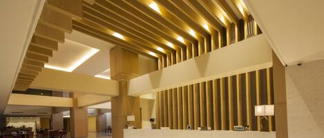 A spacious lobby with a high ceiling, a reception desk, and a seating area with tables and chairs.