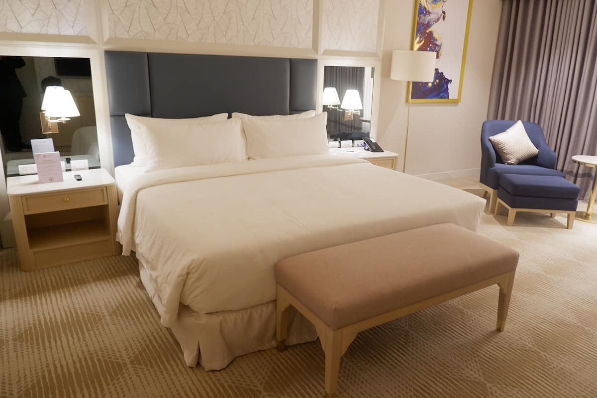 A hotel room with a large bed, bedside tables with lamps, a blue armchair, and a small round table.
