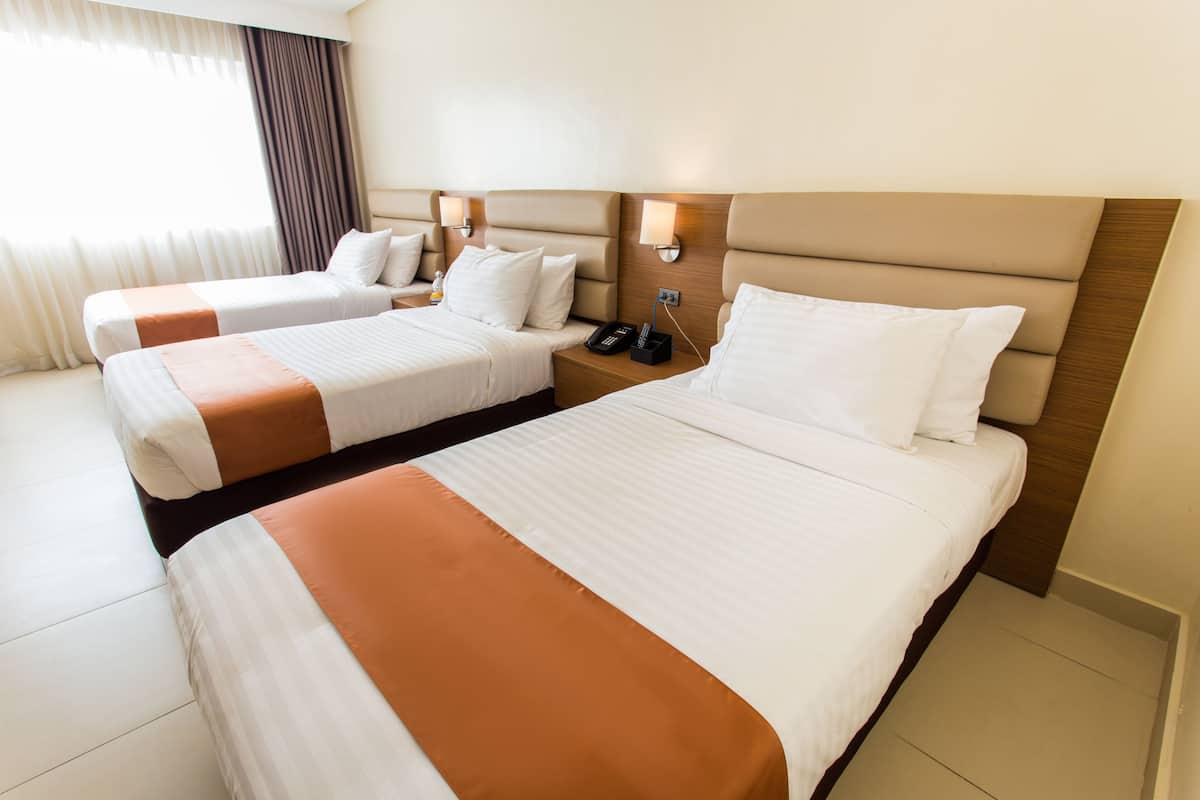 A hotel room with two beds, each with a headboard, bedside tables, and lamps.
