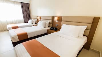 A hotel room with two beds, each with a headboard, bedside tables, and lamps.