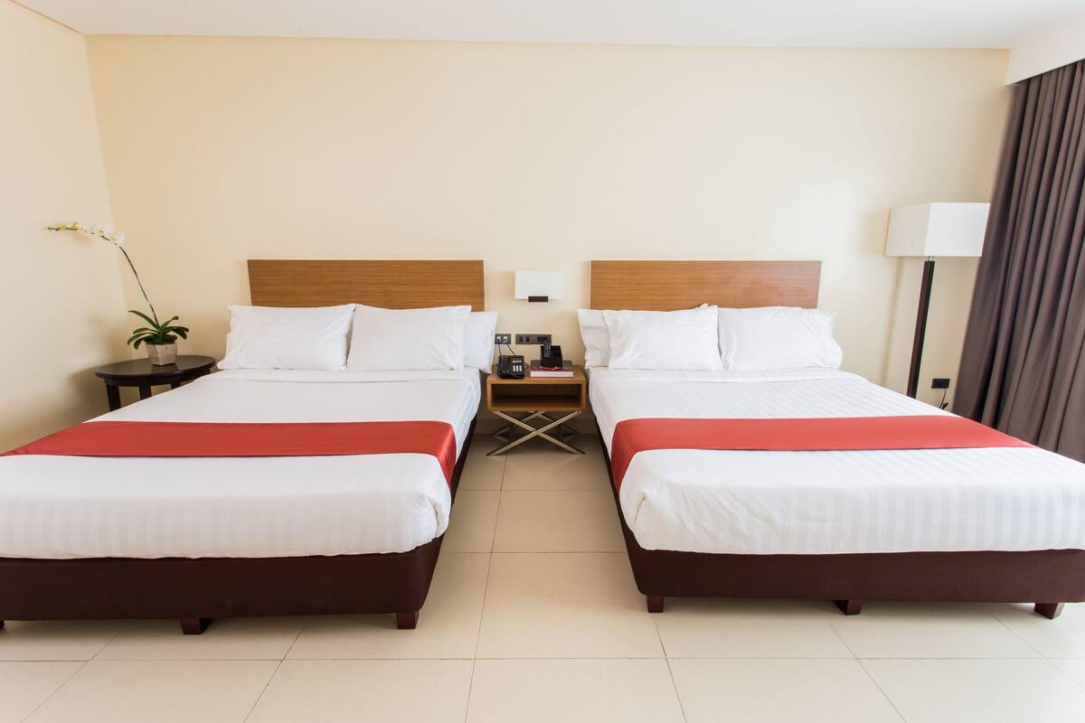 A hotel room with two beds, a nightstand, a lamp, and a potted plant.