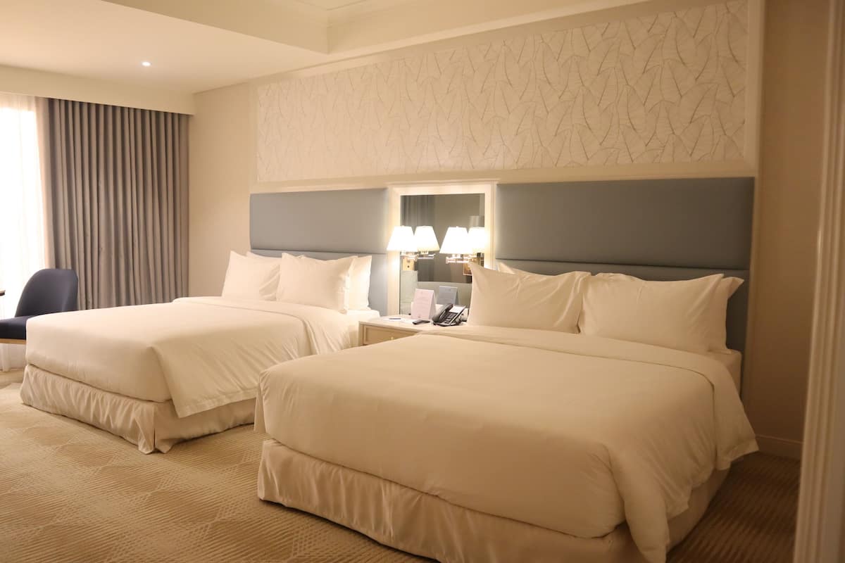 A hotel room with two beds, a desk, a chair, and a window with curtains.
