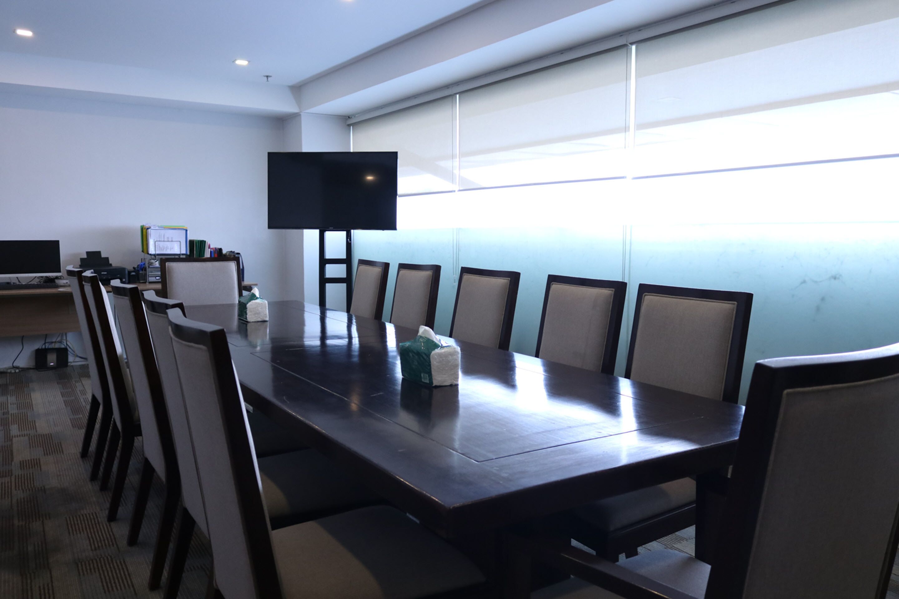 A conference room with a long table, chairs, a flat-screen TV, and a whiteboard.