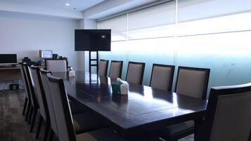 A conference room with a long table, chairs, a flat-screen TV, and a whiteboard.