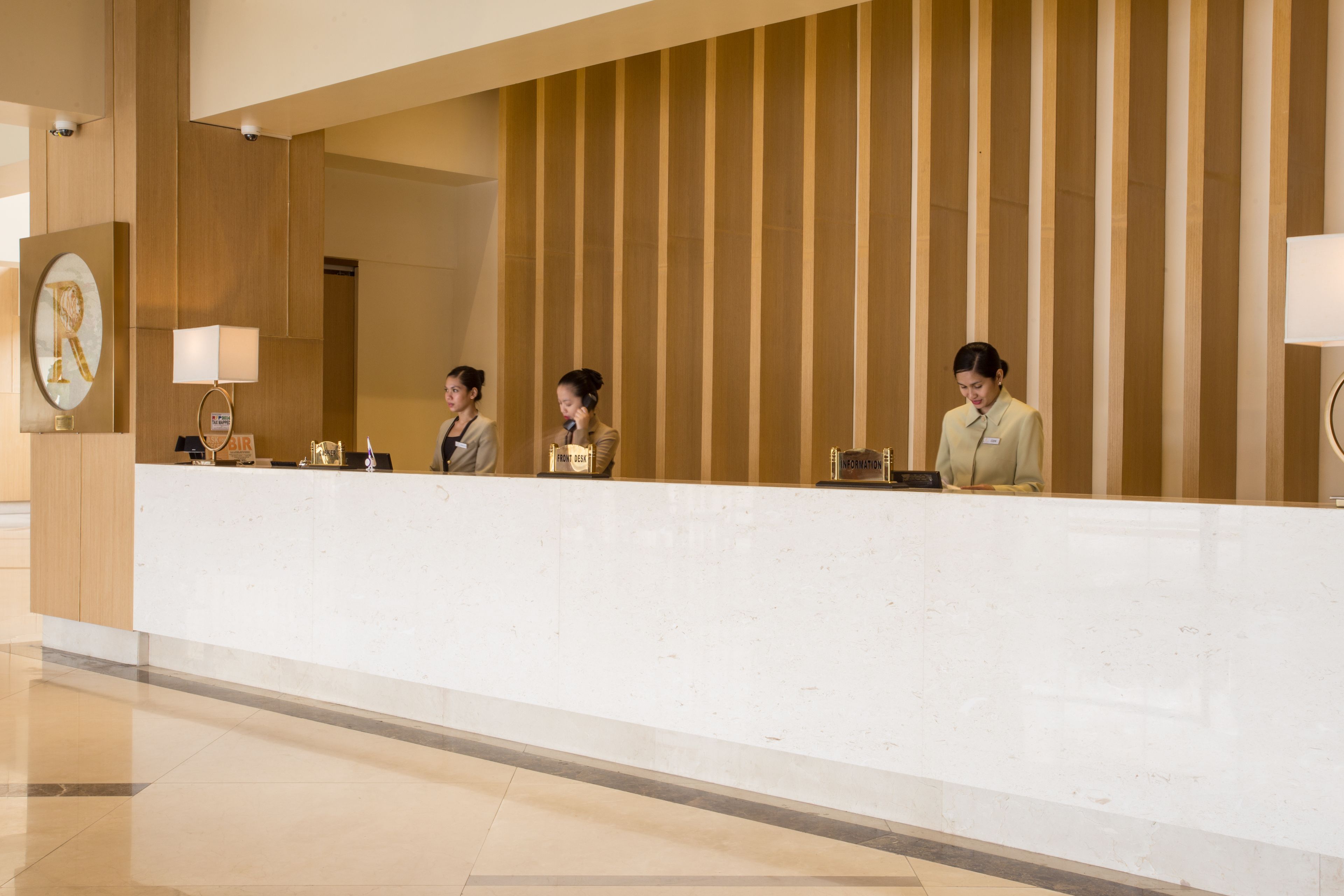 A reception desk with three staff members, a wooden panel wall, and a marble-framed artwork.