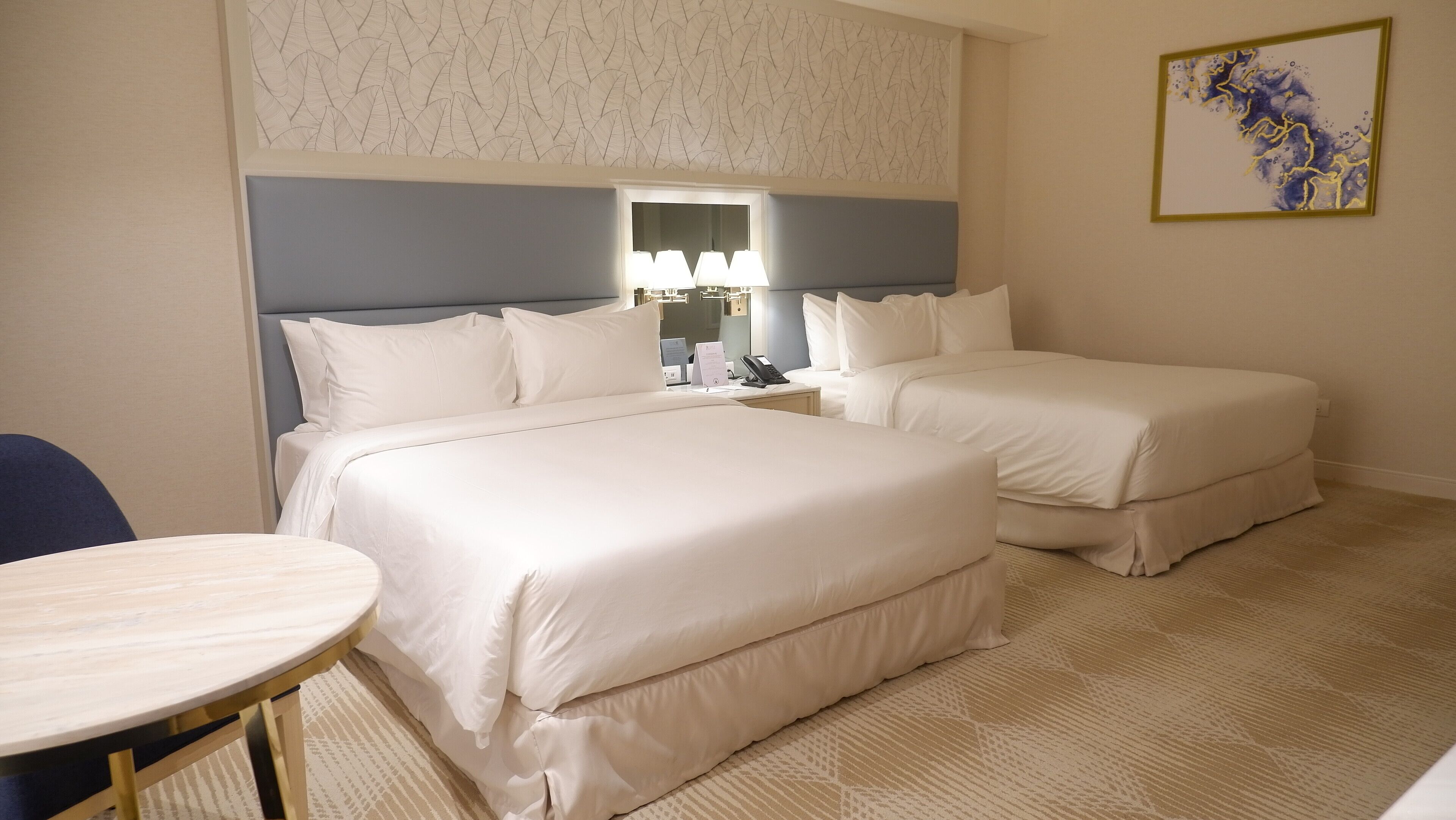 A hotel room with two beds, a desk, and a chair.