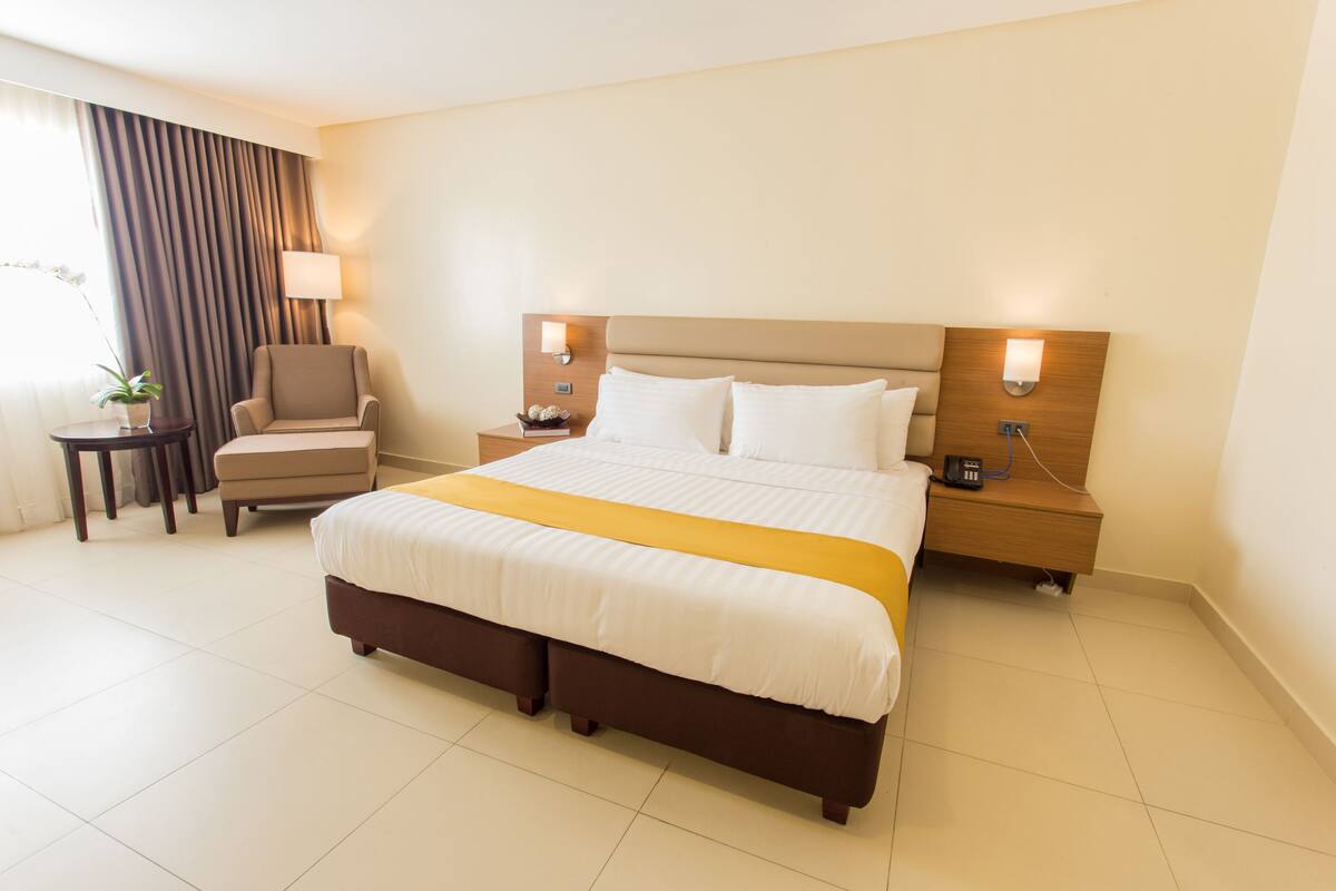 A hotel room with a large bed, a chair, a nightstand, and a lamp.