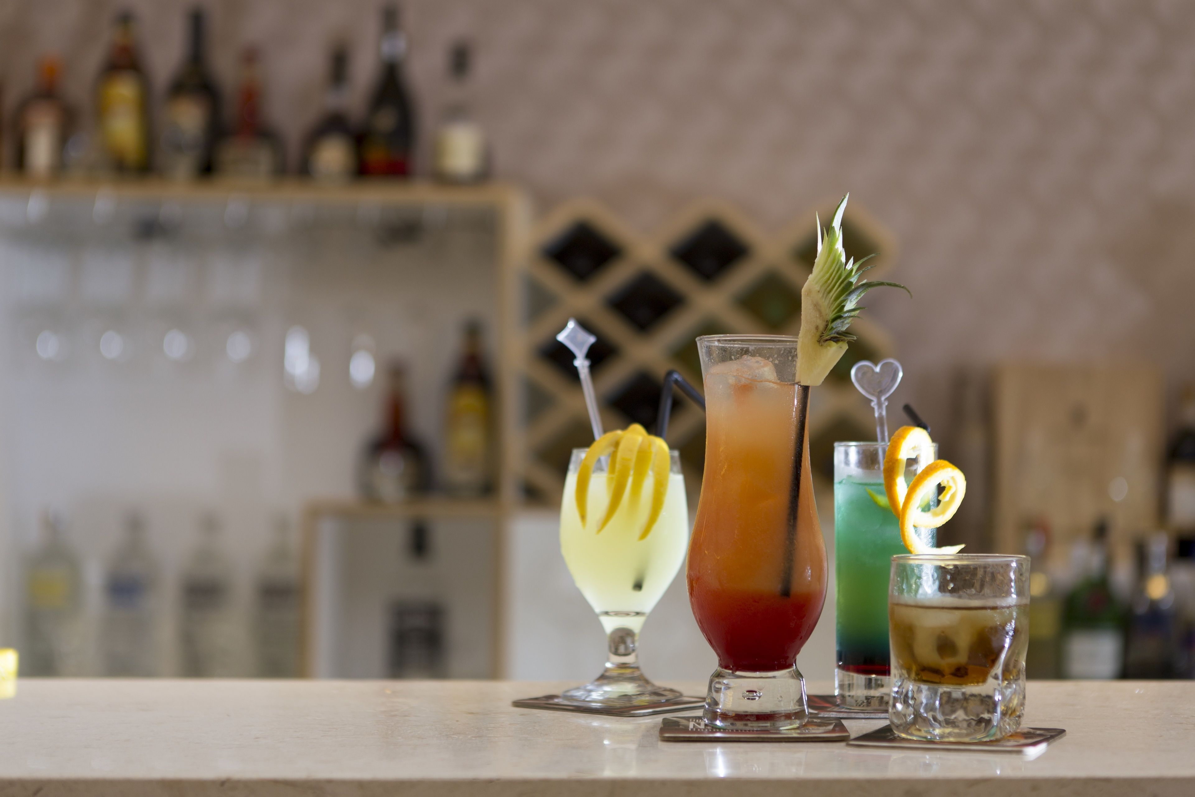 A bar counter with three different cocktails, each garnished with a lemon slice and a sprig of rosemary.