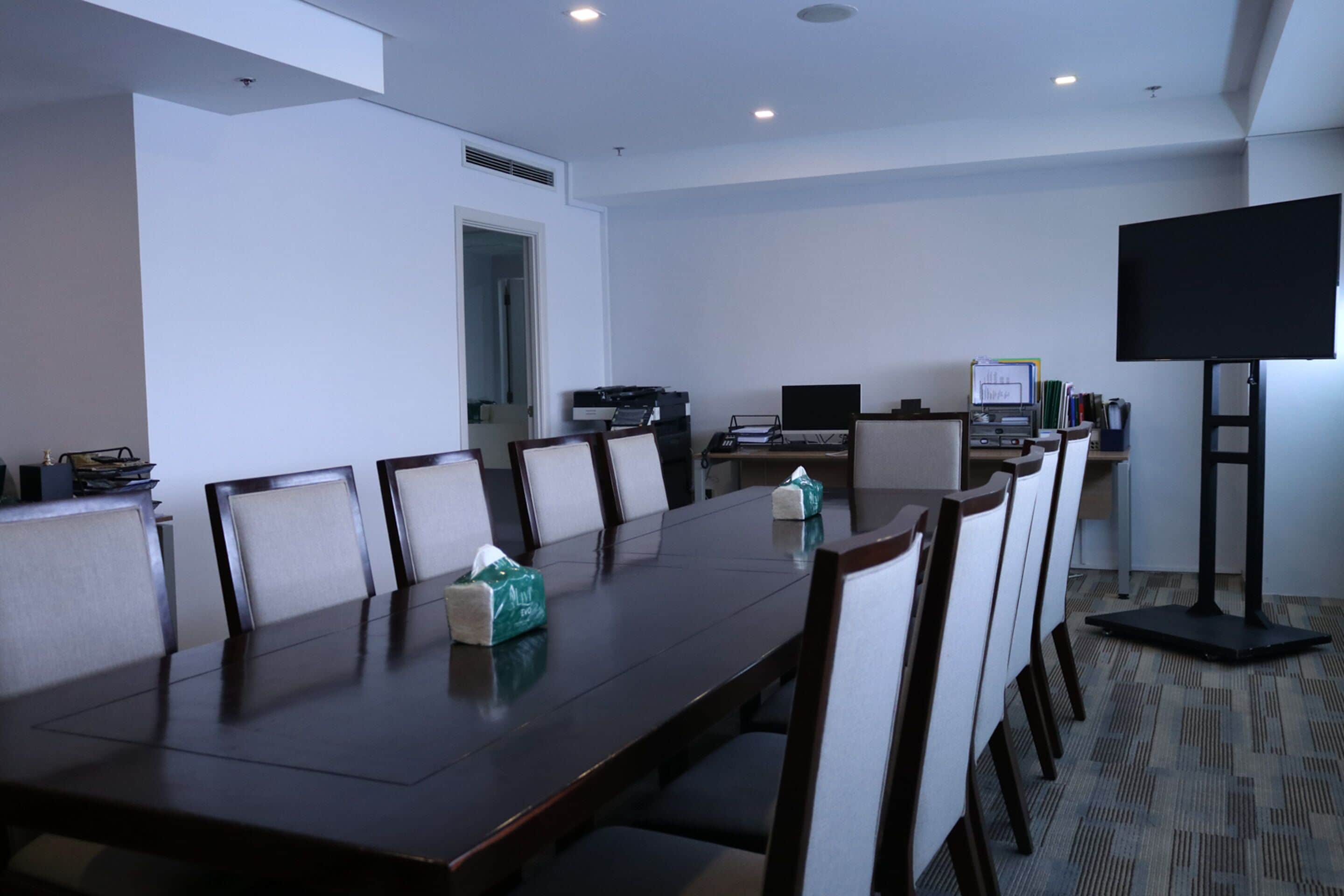 A conference room with a long table, chairs, a television, and a computer setup.