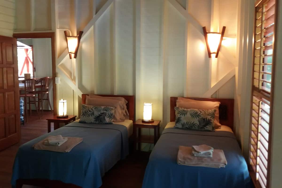 A hotel room with two beds, each with a nightstand and a lamp. There is a staircase leading to another room.