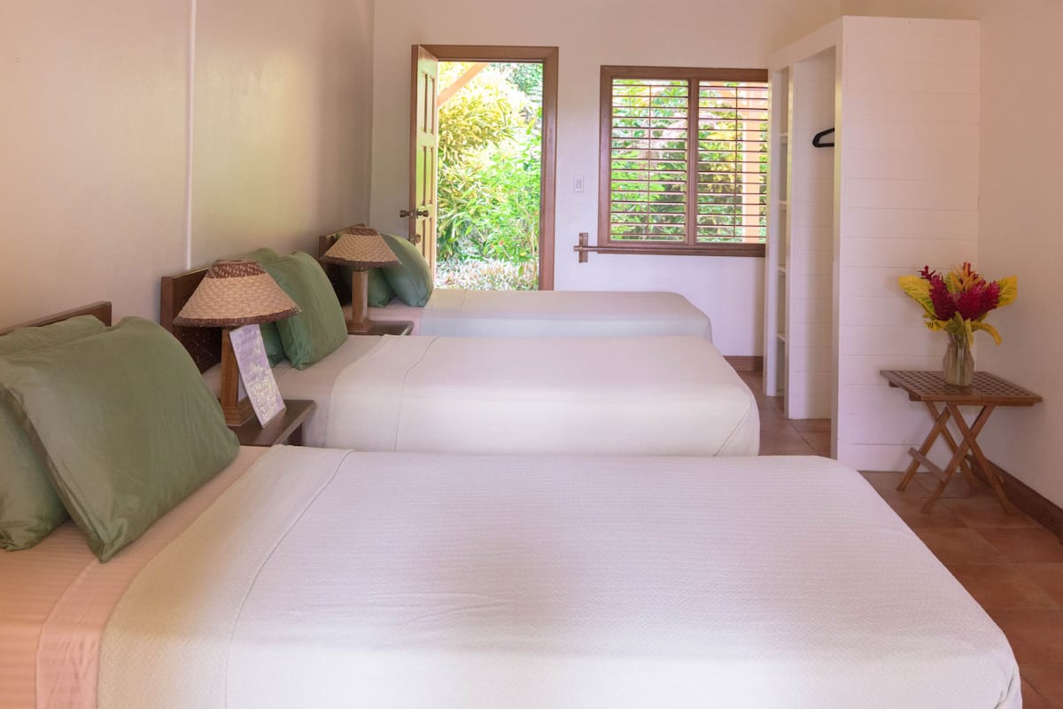 A hotel room with two beds, a small table with a lamp, and a window with blinds.