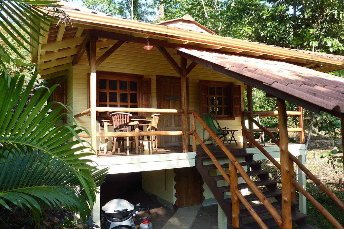 A wooden cabin with a porch, outdoor seating, and a water heater.