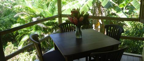 Une table en bois, entourée de chaises, et un vase rempli de fleurs, le tout installé sur un balcon offrant une vue sur une végétation luxuriante.