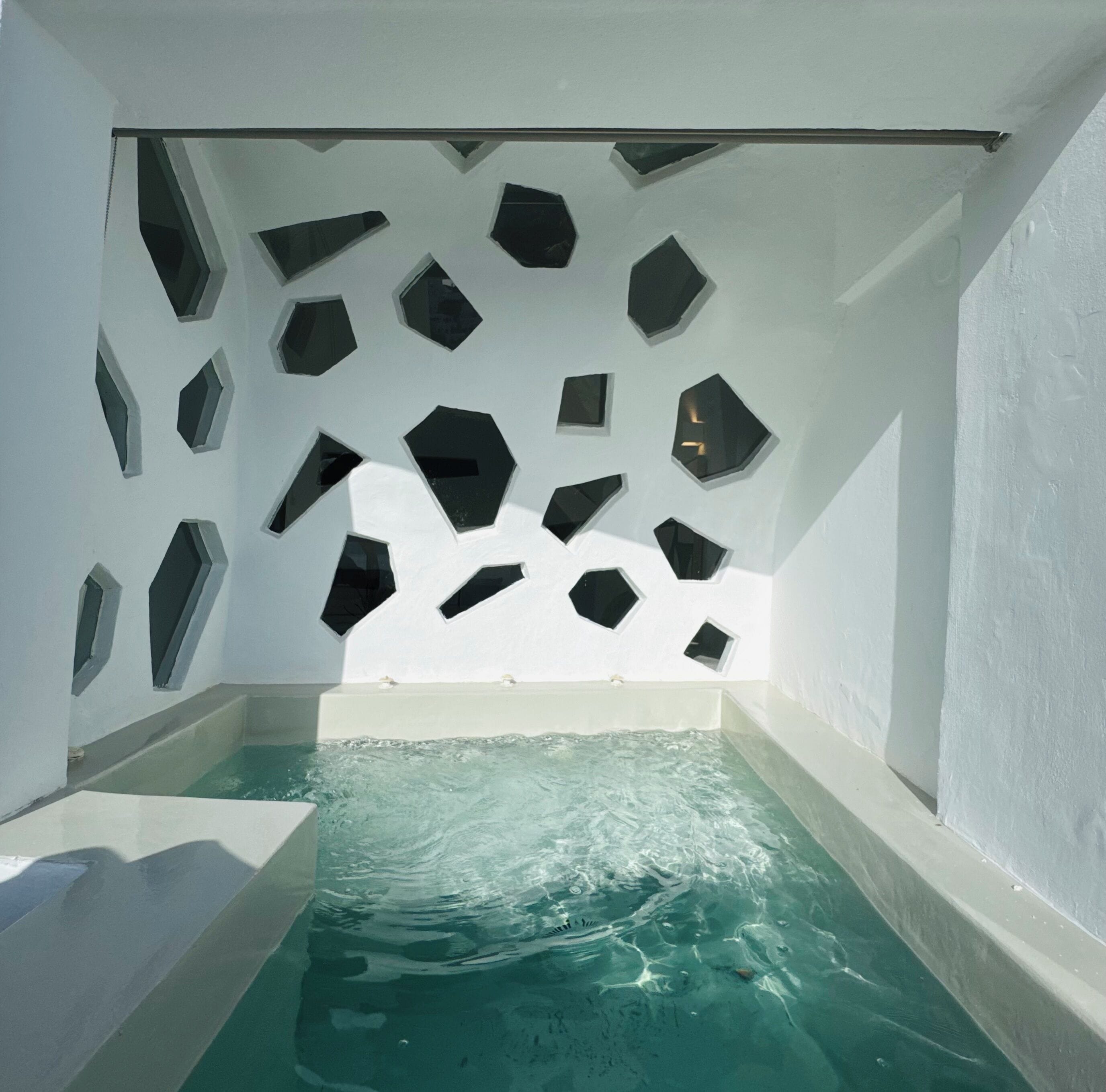 A modern spa with a geometric wall design, a clear pool, and a white interior.