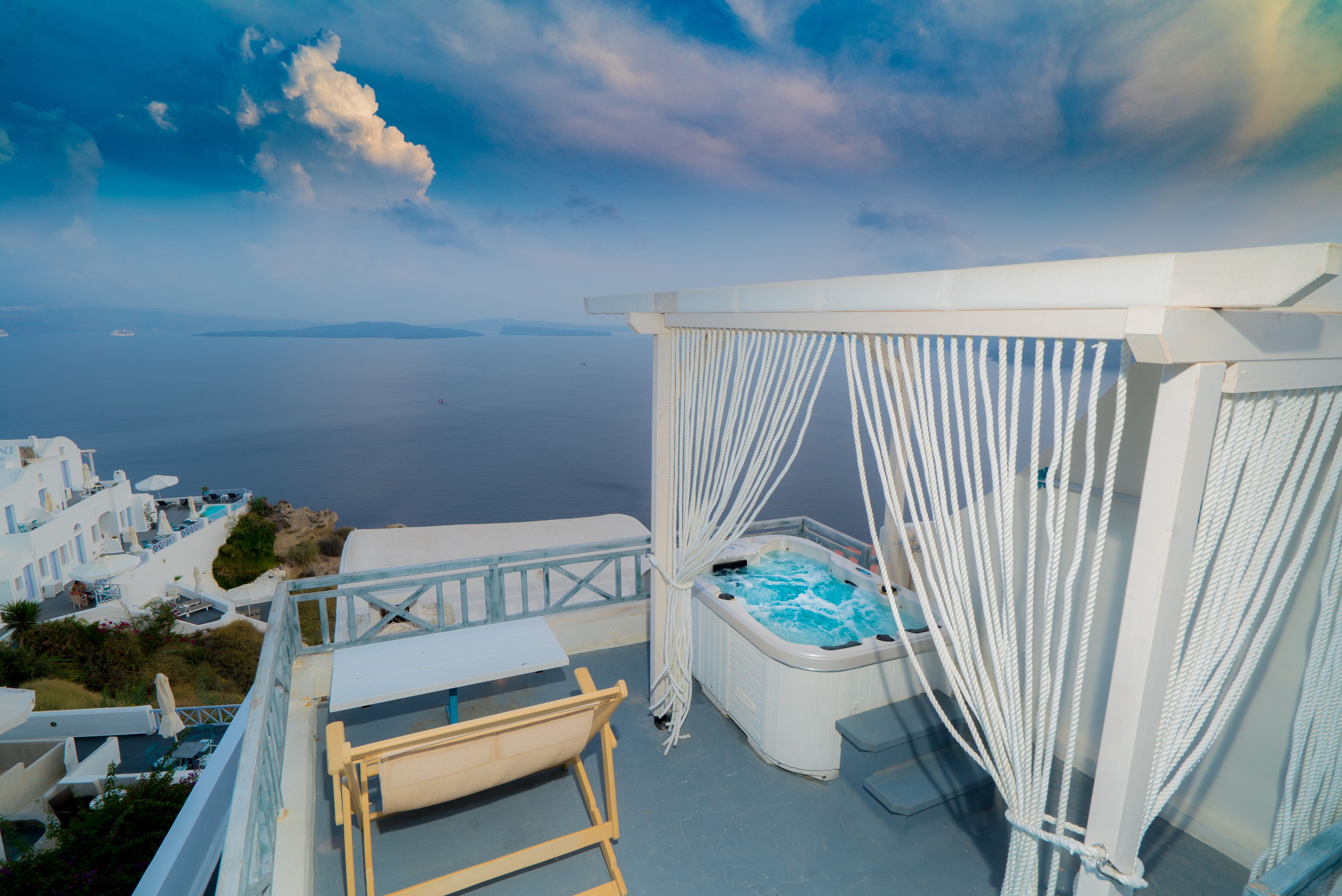 Un balcón con jacuzzi, cortinas blancas y vista al mar.