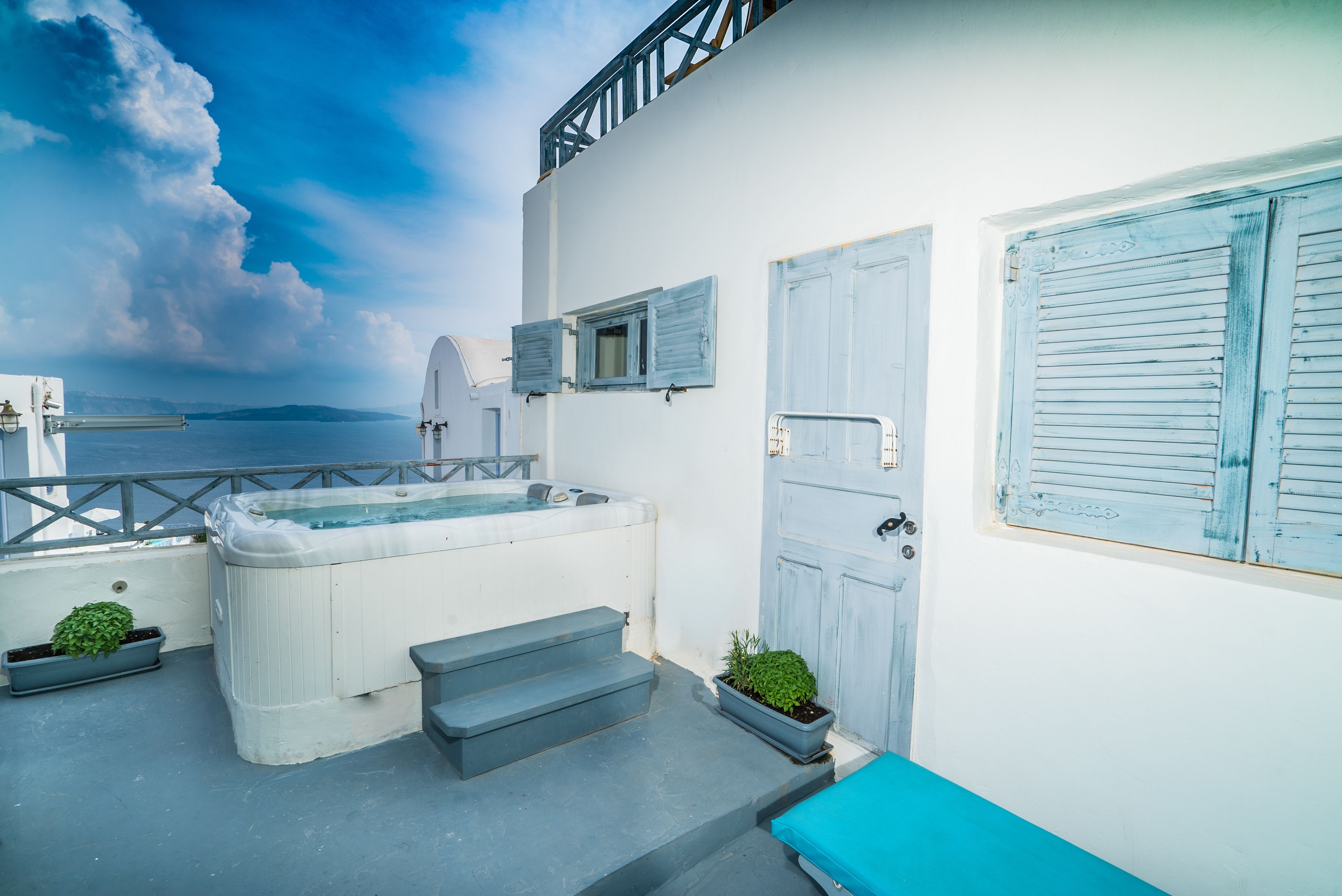 A white building with a hot tub, steps leading to a door, and a view of the sea.