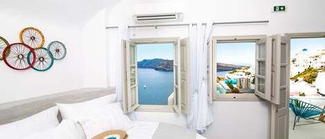 A bedroom with a bed, a view of the sea, and a window with a view of a white building.