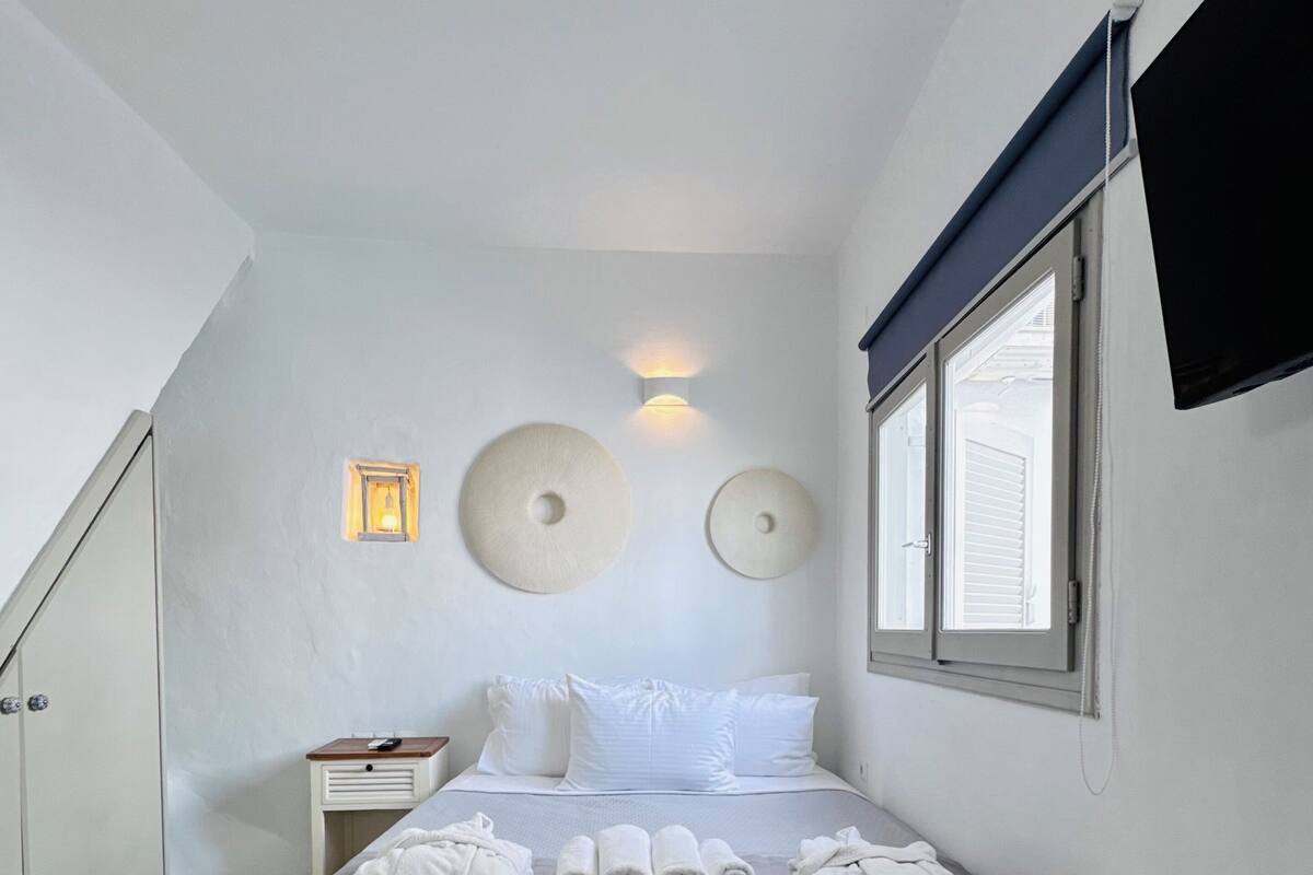Een slaapkamer met een bed, nachtkastjes, een aan de muur bevestigde televisie en een raam.
