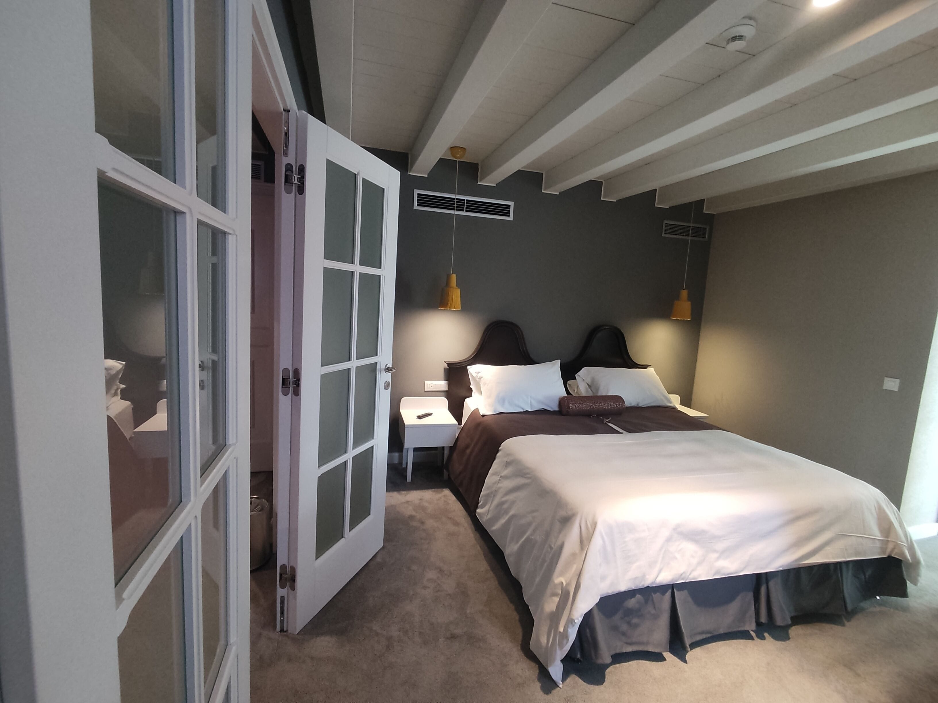 A bedroom with a bed, bedside tables, a nightstand, a lamp, and a door leading to another room.