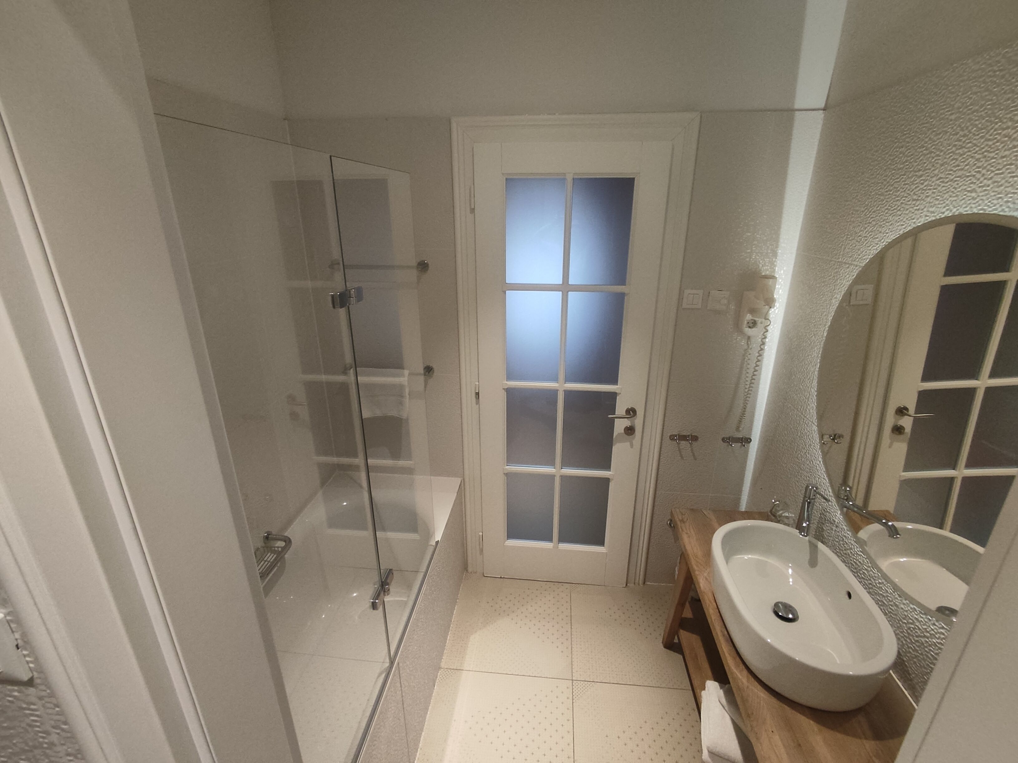 A bathroom with a glass-enclosed shower, a white door with frosted glass panels, and a wooden vanity with a large mirror.