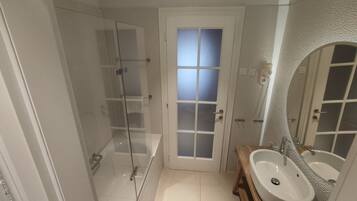 A bathroom with a glass-enclosed shower, a white door with frosted glass panels, and a wooden vanity with a large mirror.
