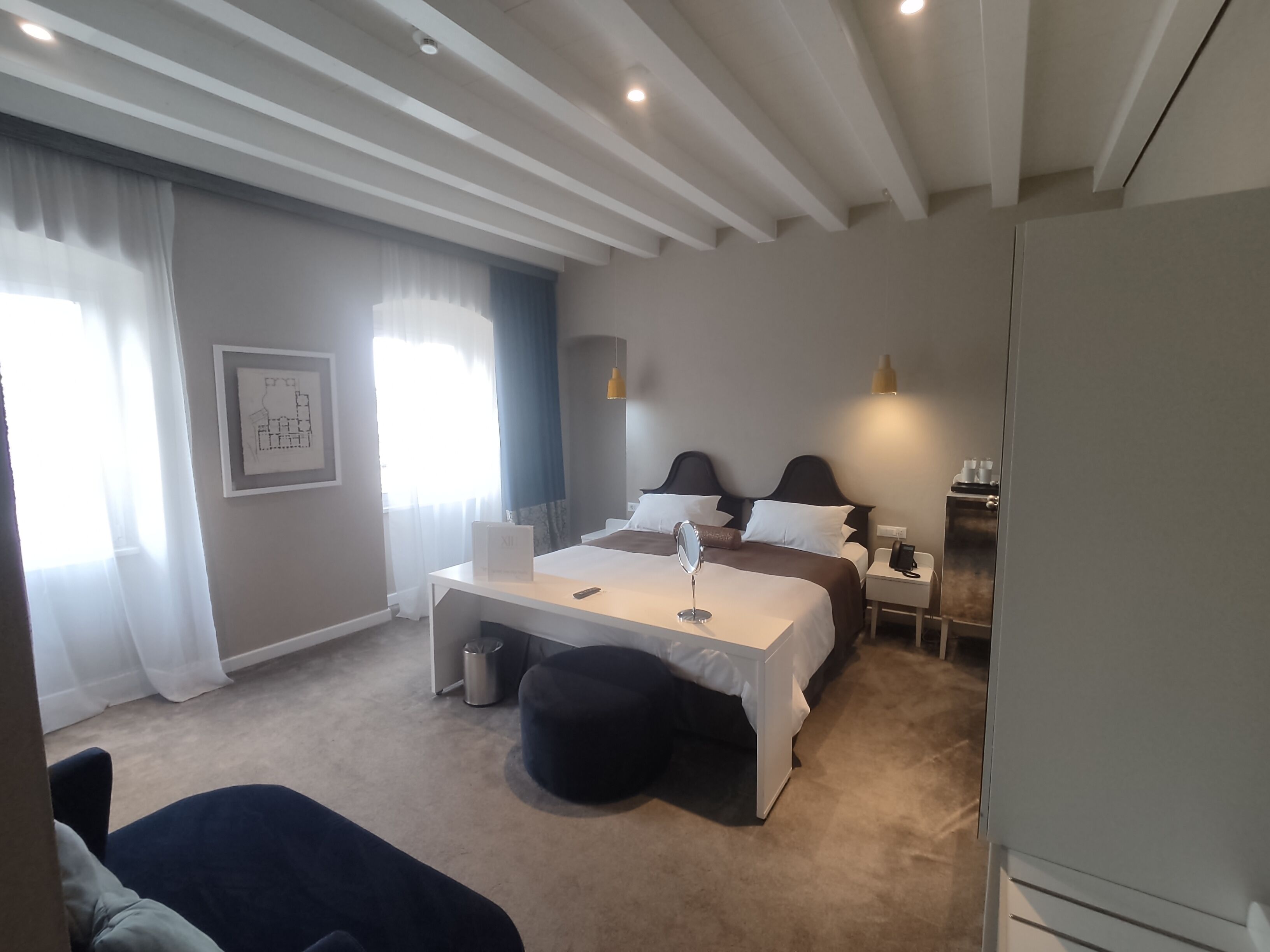 Una habitación de hotel con cama, mesita de noche, lámpara y un pequeño escritorio.