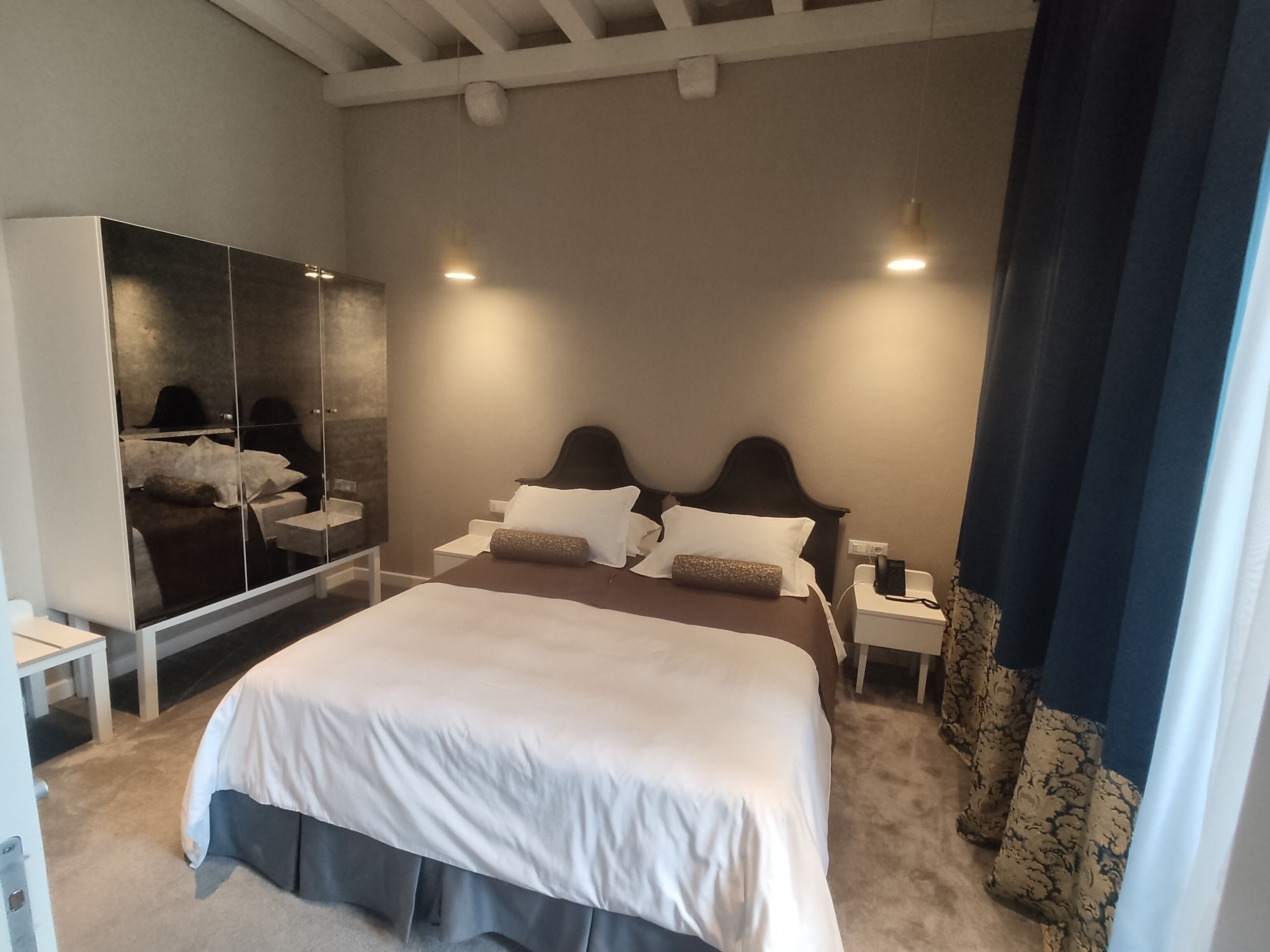 Une chambre d’hôtel moderne avec un grand lit, une armoire, une table de chevet et une petite table de nuit.