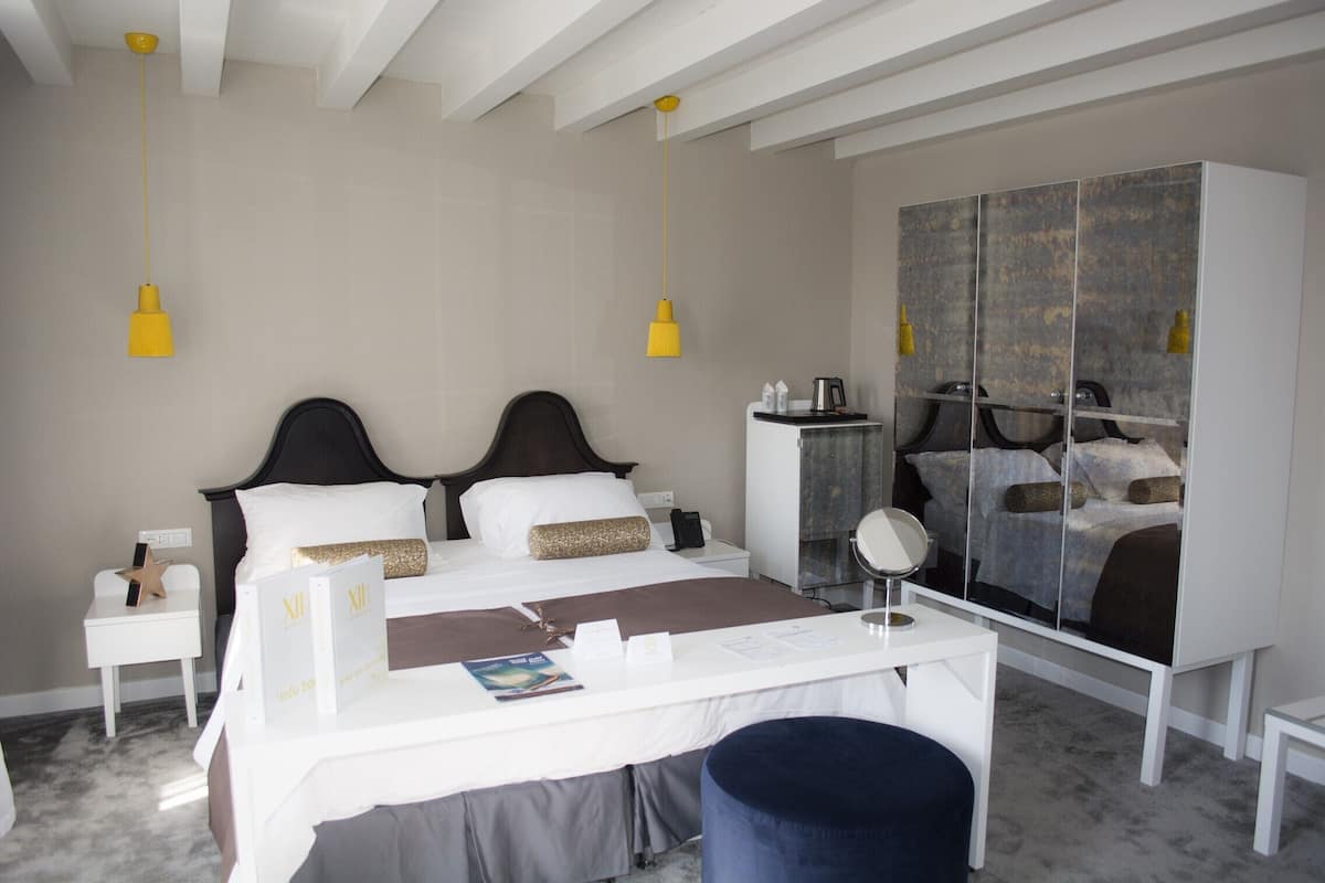 A hotel room with a bed, bedside tables, a desk, a chair, a wardrobe, and a mirror.
