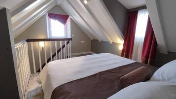 A bedroom with a sloped ceiling, a bed with white and brown bedding, a window with red curtains, and a staircase with white railings.