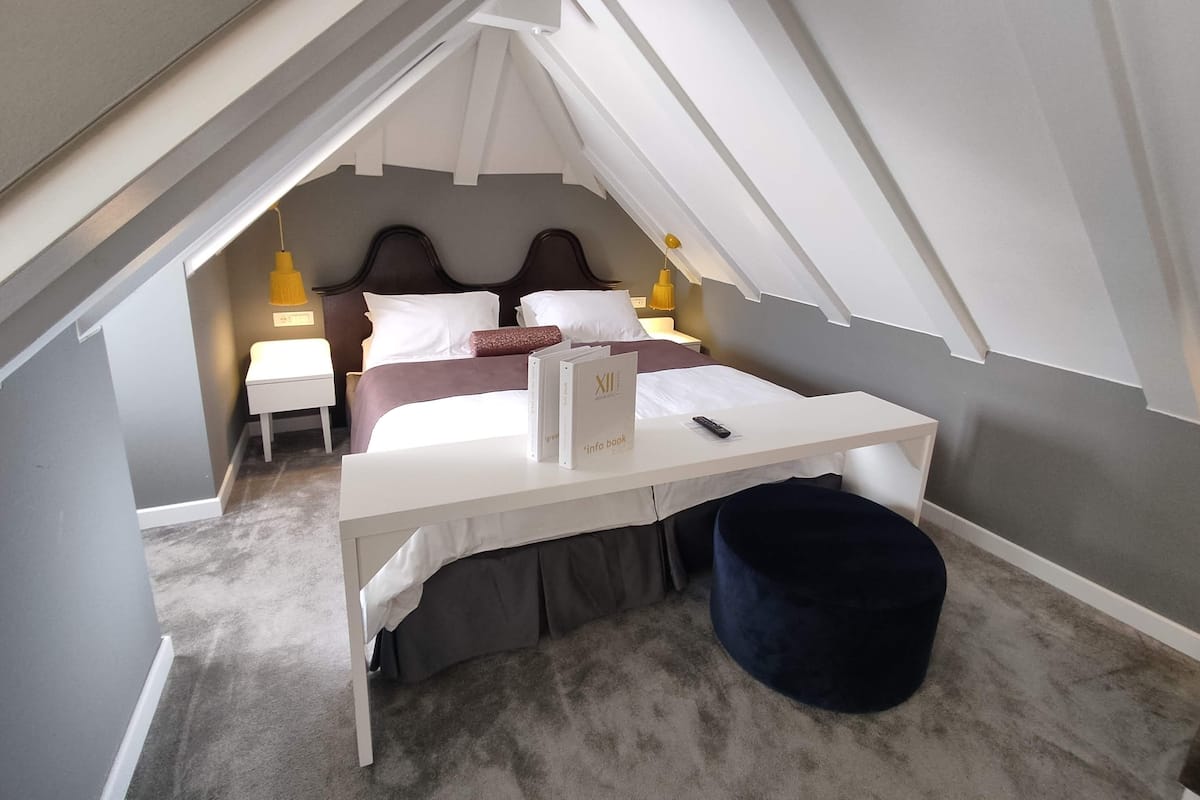 A small, triangular attic bedroom with a bed, bedside tables, a desk, and a chair.