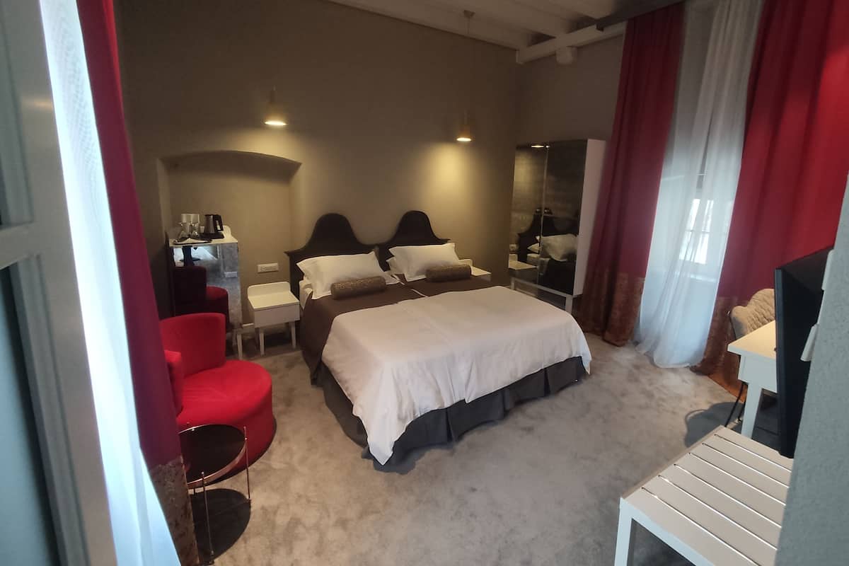 A hotel room with a large bed, a desk, a chair, and a mirror.