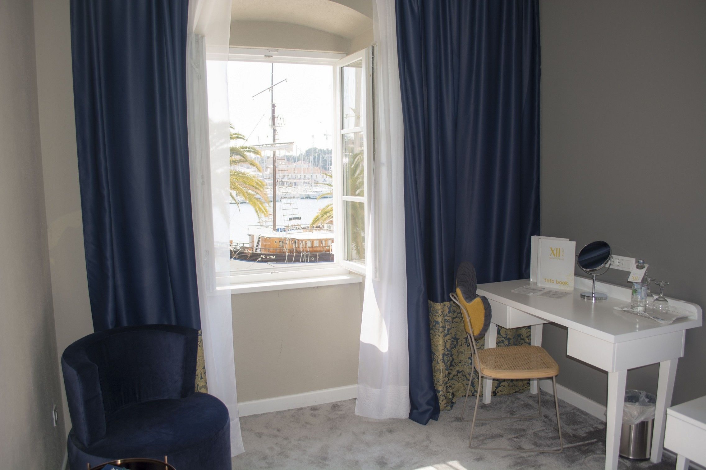 Ein Zimmer mit Schreibtisch, Stuhl und Blick auf einen Yachthafen durch ein Fenster.