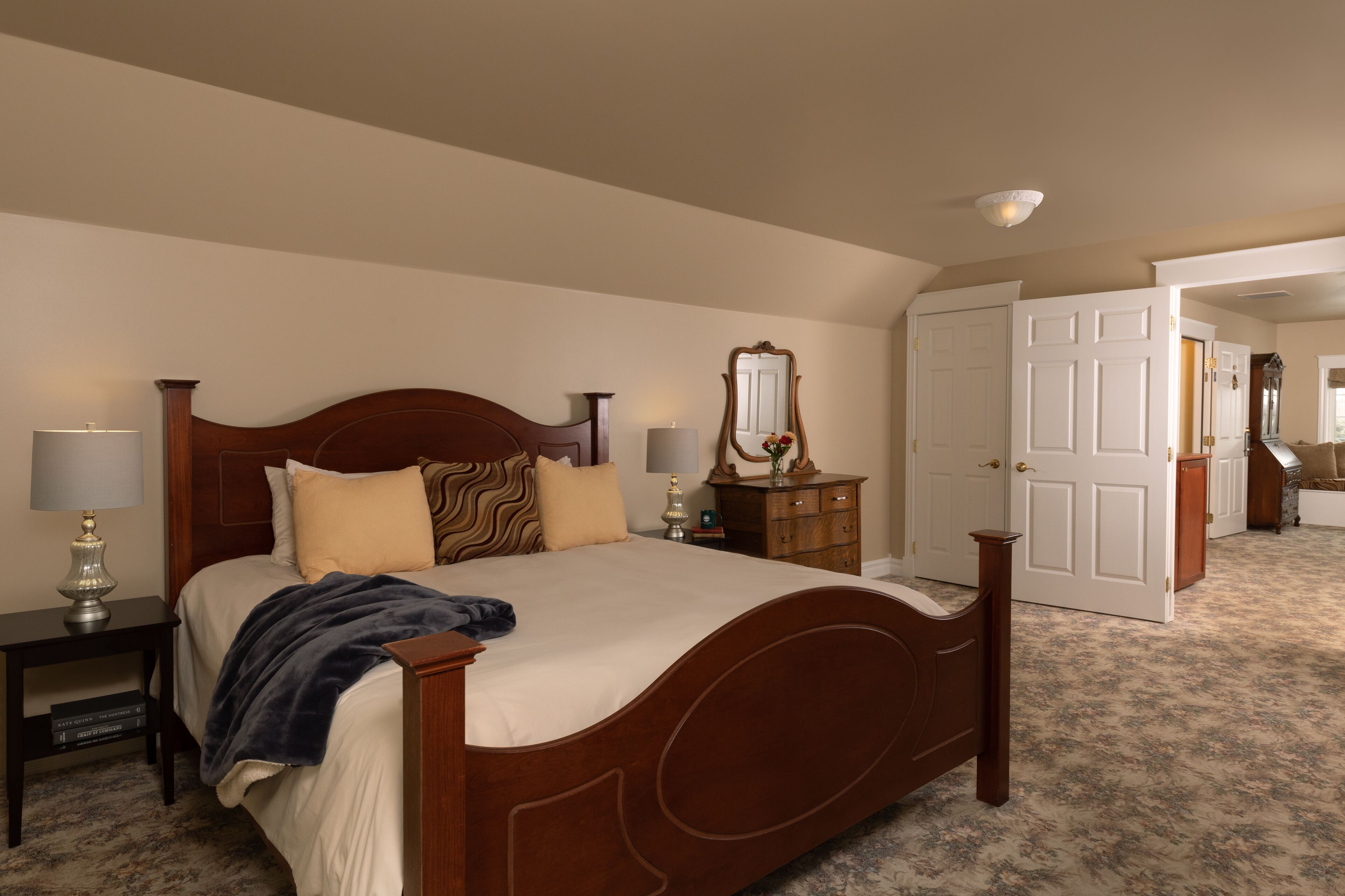 Uma cama bem arrumada com cabeceira de madeira, uma mesa de cabeceira com abajur e um penteado com espelho.
