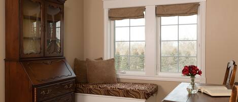 A room with a built-in bench at a window, a wooden dresser, and a table with a vase of flowers.
