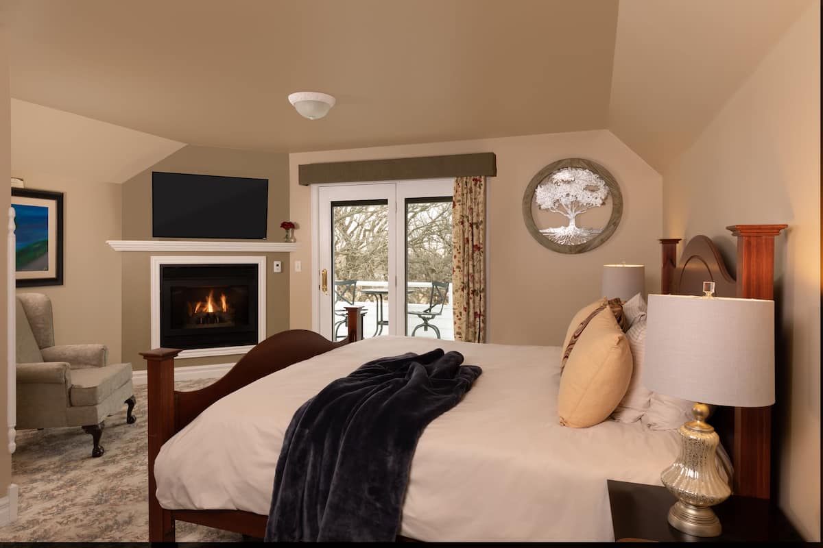 Un dormitorio con chimenea, una cama con manta oscura, una lámpara y vistas al exterior.