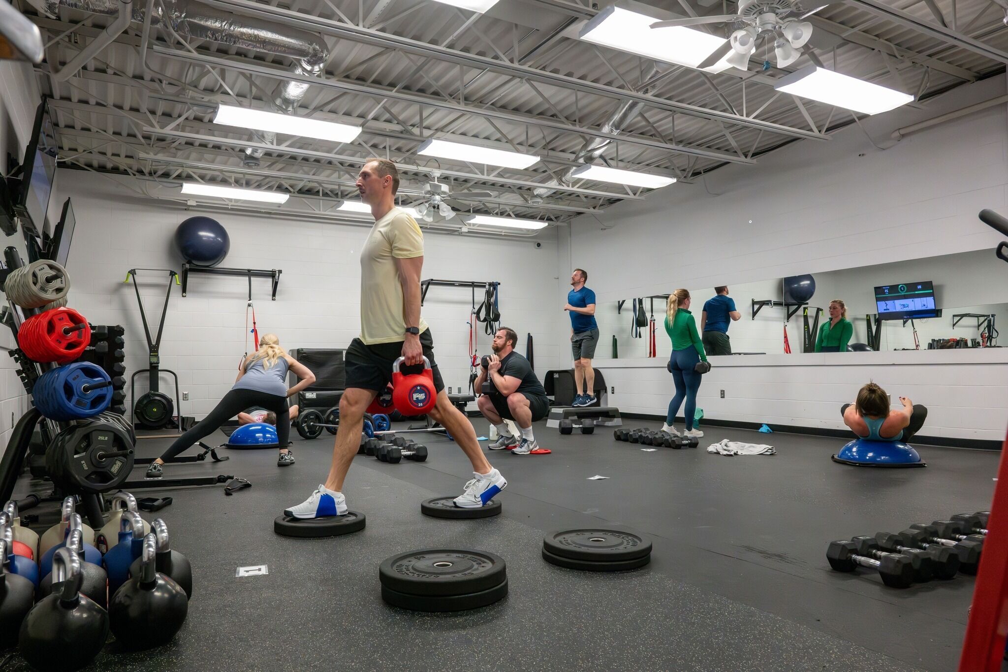Une salle de sport équipée de divers appareils d’entraînement, notamment des kettlebells, des haltères et des ballons d’exercice.