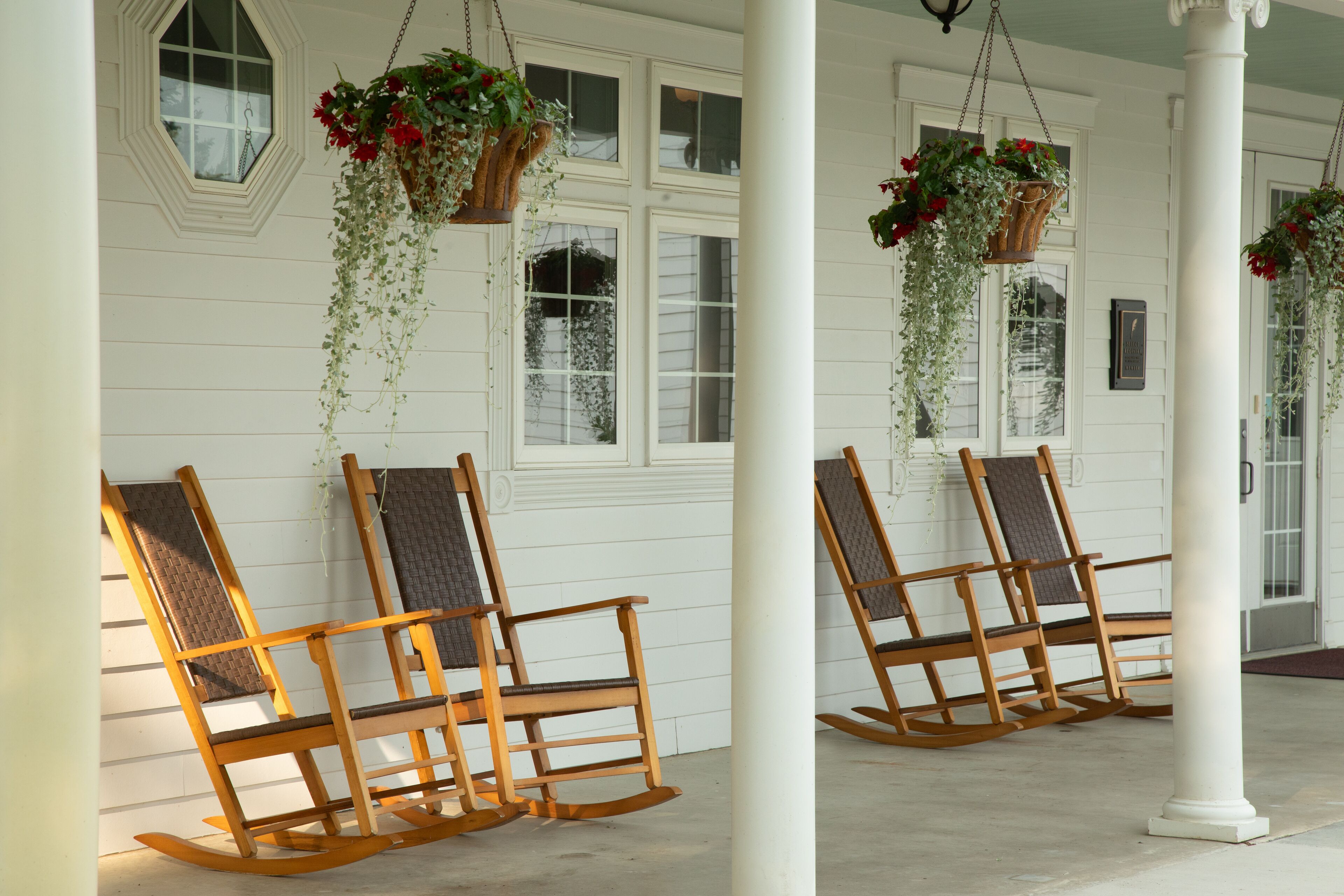 A porch with two rocking chairs and hanging flower baskets.