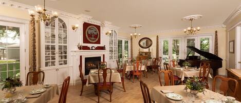 A dining room with multiple tables set for a meal, a grand piano, and a fireplace.