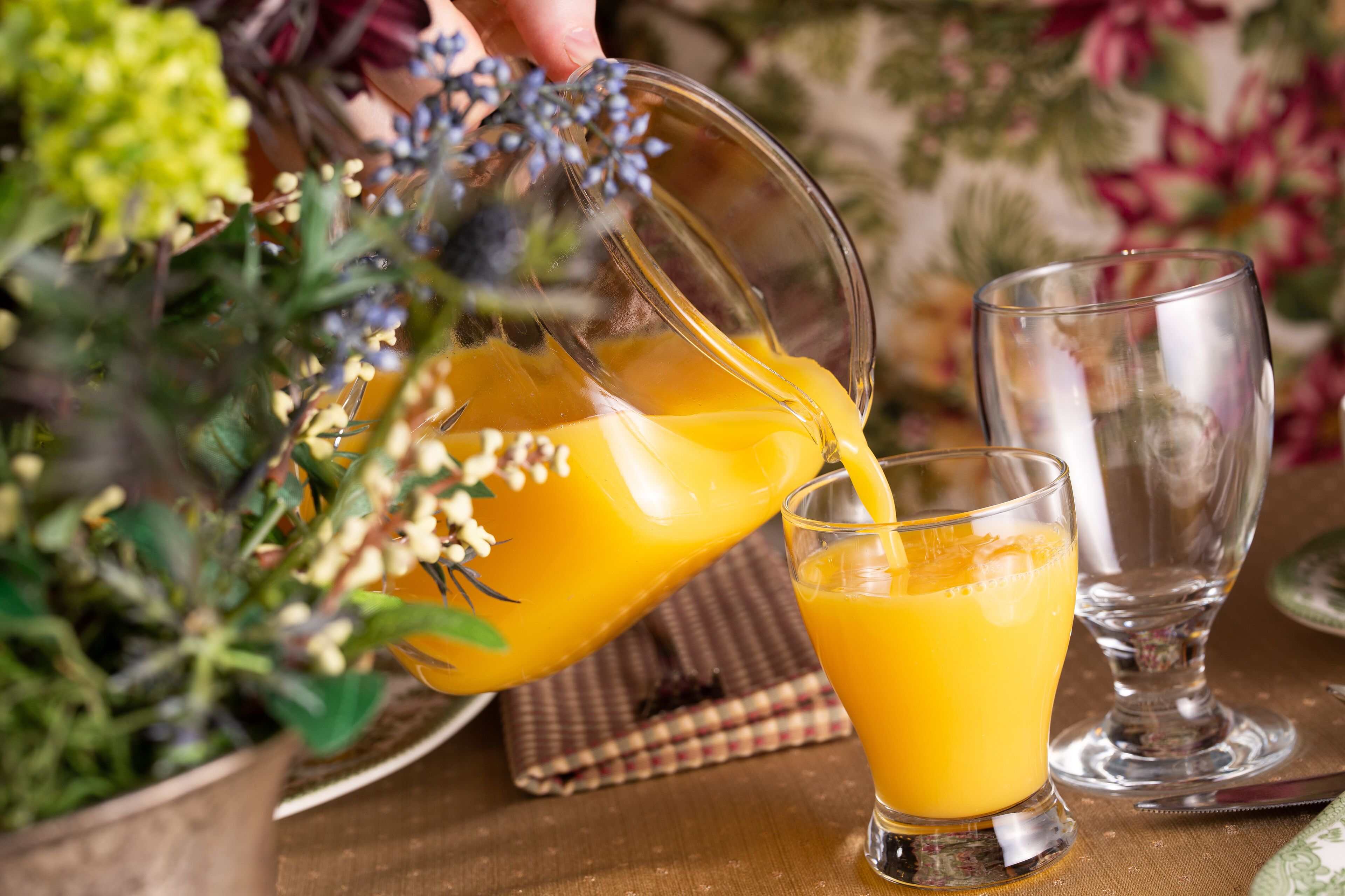 Une main versant du jus d’orange dans un verre.