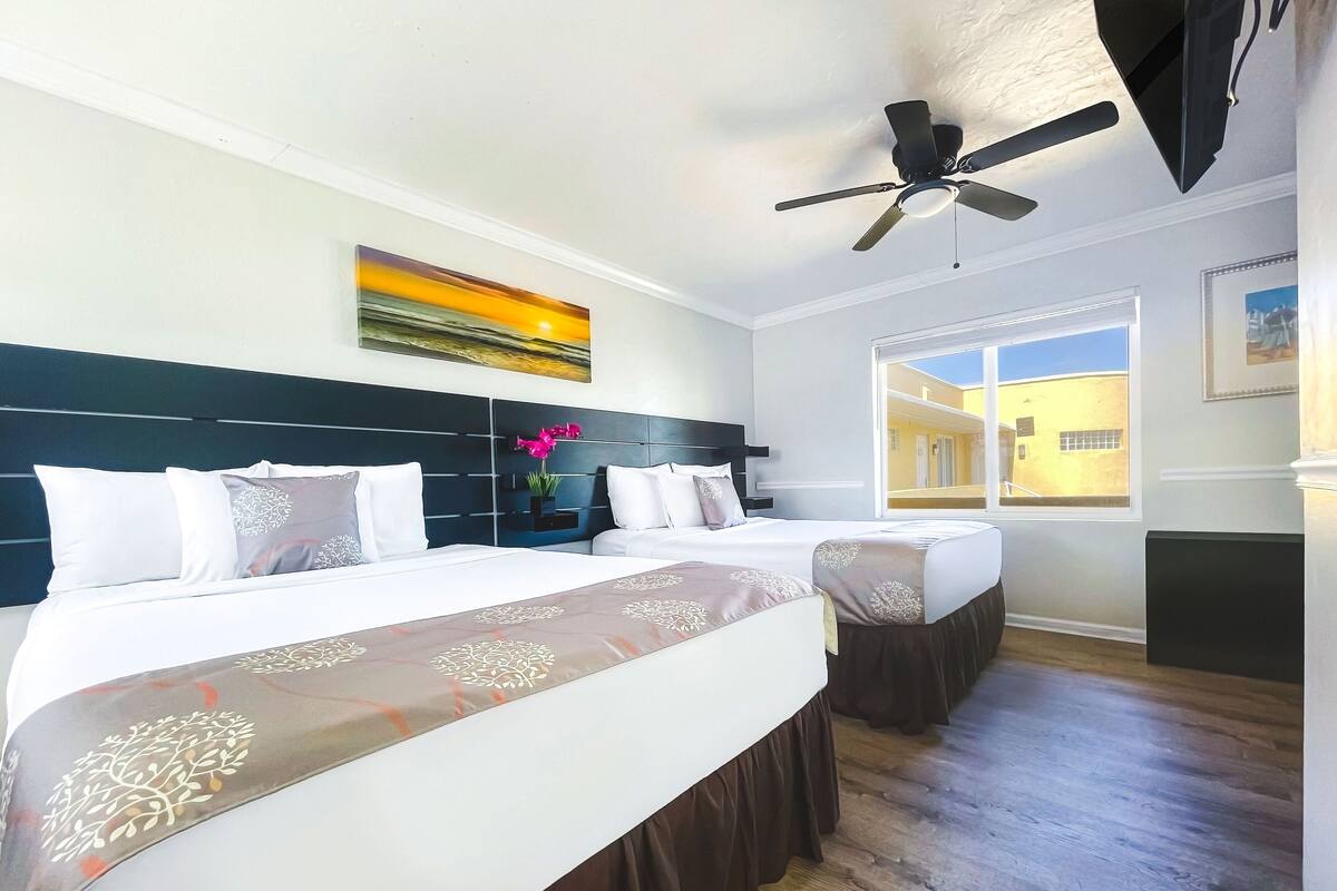 Une chambre d’hôtel avec deux lits, un ventilateur de plafond, un tableau et une vue sur l’extérieur.