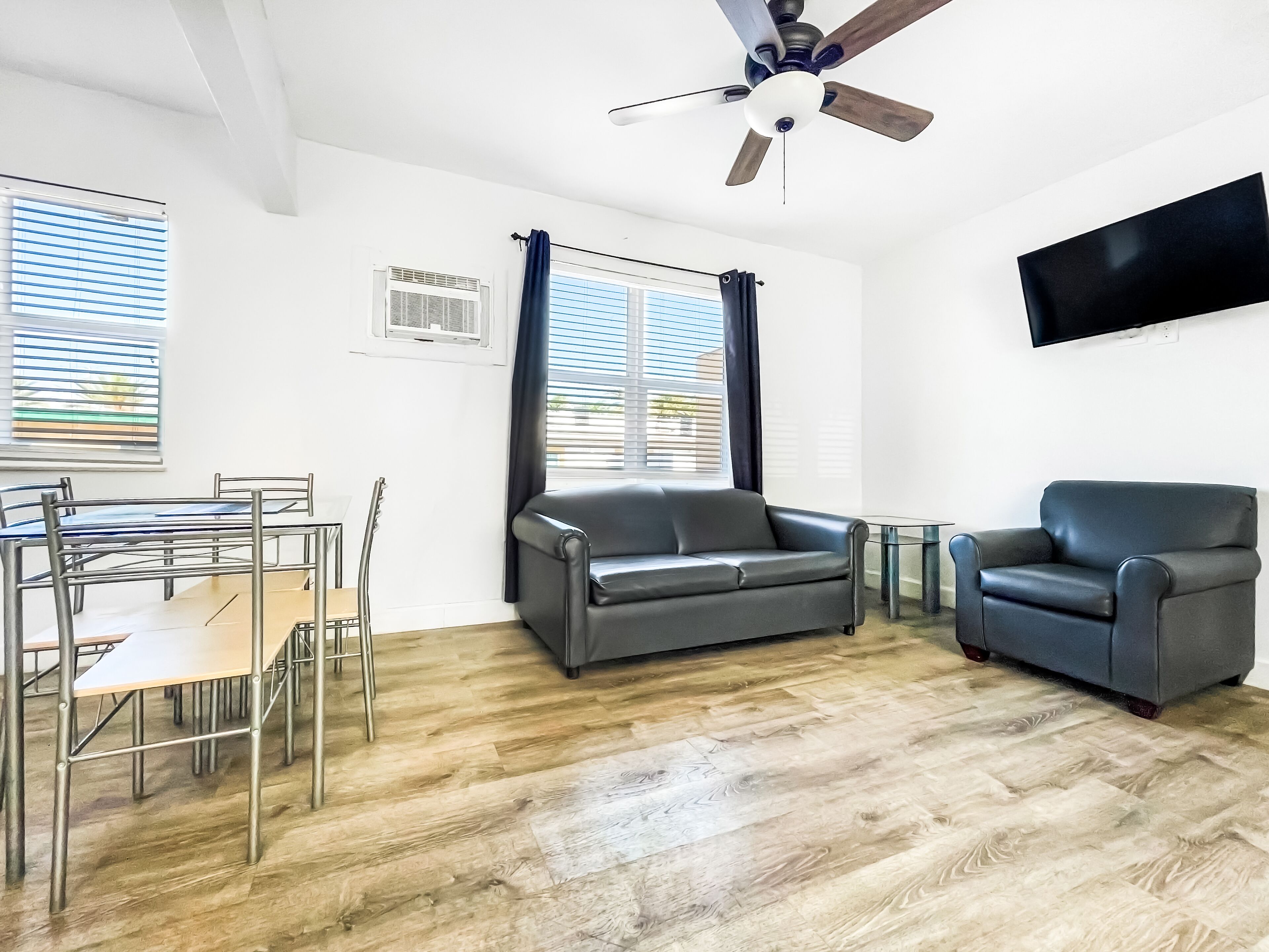 Un salon moderne comprenant un coin repas, un ventilateur de plafond et un téléviseur à écran plat fixé au mur.