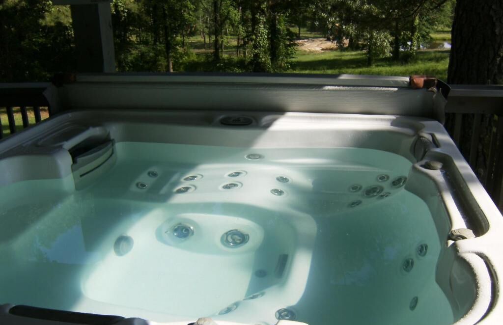 A hot tub with multiple jets, surrounded by a wooden deck and trees in the background.