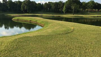 A golf course with a pond, trees, and a clear sky.