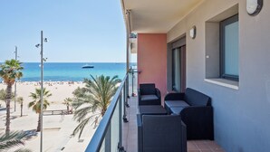 Een balkon met rieten meubilair, uitzicht op het strand en een helderblauwe lucht.