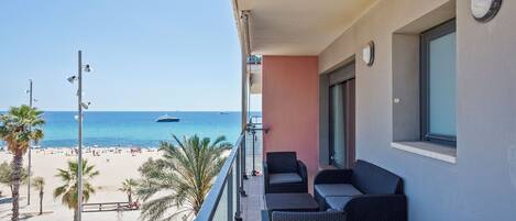 A balcony with wicker furniture, a view of the beach, and a clear blue sky.