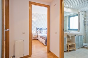 Un corridoio che conduce a una camera da letto con un letto, un comodino e una finestra. La stanza ha un pavimento in legno e un termosifone.