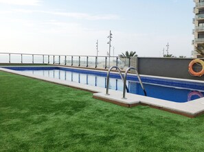 Una piscina con una scala in metallo, circondata da un prato e un parapetto metallico.
